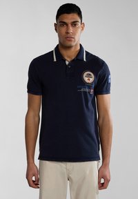 Námořnická modrá polo tričko s kontrastním límcem a vyšitým logem. Krátké rukávy a boční rozparky na spodním lemu. Bavlněný materiál.