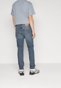 Blå denimjeans, rak passform, två bakfickor och läderlapp. Matchas med en ljusgrå T-shirt med kort ärm och grå sneakers.