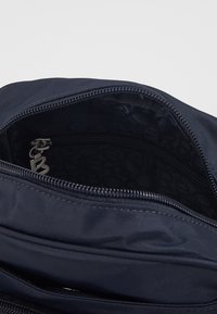 Granatowa torba materiałowa z otwartym zamkiem odsłaniającym wewnętrzną kieszeń i czarną podszewką z wzorzystym tekstem.