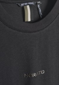 Close-up crnog majice s okruglim izrezom s logotipom "MORATO" centriranim ispod izreza vrata i oznakom "ANTONY MORATO" unutar ovratnika, veličina srednja.