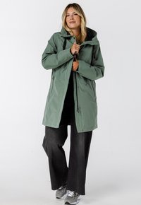 Lichtgroene, waterdichte parka met een capuchon, ritsvoorzijde en aantrekkoorden. Voorzien van zijzakken en een zwart gevoerde binnenkant.