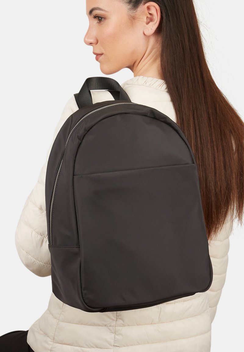 Mochila negra hecha de nylon suave, de forma redondeada, con cierre de cremallera y asas cortas para llevar. Diseño simple, sin patrones visibles.