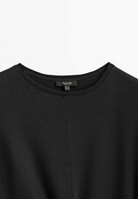 Haut noir à manches courtes avec un col rond, fabriqué en tissu lisse. Comprend une couture centrale discrète et une étiquette indiquant la taille.