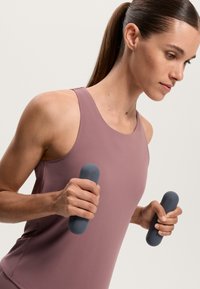 Light pink athletic tank top with wide straps; gray handheld weights in each hand, showcasing a smooth surface and rounded ends.
