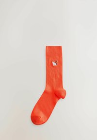 Chaussette orange vif avec un petit lémur brodé près du haut, affichée sur un fond gris clair.