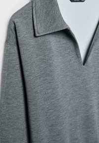 Grå polo-stil top med en bred krave, der har en V-formet halsudskæring. Blødt, struktureret stof. Lange ærmer med syede sømme.