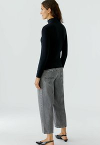Schwarzes Langarmoberteil und graue weite Jeans. Das Oberteil hat einen hohen Kragen. Die Hose hat eine ausgewaschene Textur mit Gesäßtaschen. Schwarze Ballerinas.