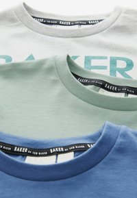 Tri majice složene jedna na drugu; boje: siva s svijetloplavim otiskom, svijetlozelena i plava. Sve imaju okrugle izreze i oznake s natpisom "BAKER by Ted Baker."