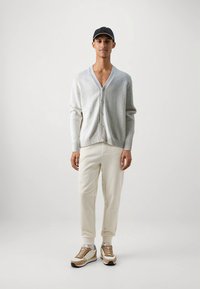 Svetlosivý kardigán s výstrihom do V a zapínaním na gombíky, doplnený béžovými nohavicami a teniskami s hnedými detailmi. Jednoduchý dizajn, hladká textúra.