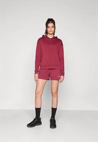 Vīnogu krāsas džemperis ar auklām, kopā ar atbilstošiem šortiem. Melni sporta apavi un vidēja garuma zeķes noslēdz sportisko tēlu.