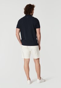 Marinblå polo med korta ärmar och krage, matchad med ljusa linnebyxor och vita sneakers. Bakifrån visad.