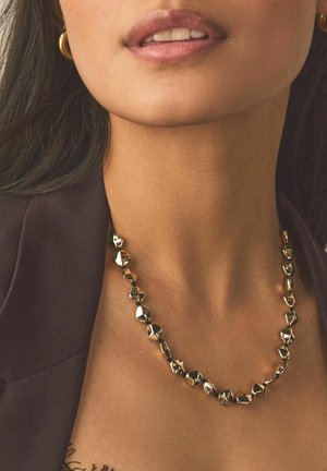 Metal necklace featuring irregular-shaped golden links with a polished finish, worn over a dark, textured top.