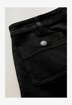 Schwarzer Denim-Stoff im Detail, der eine Nahaufnahme einer Tasche, eines Metallknopfs und der Naht zeigt. Glatte Textur mit feinem Fischgrätenmuster.