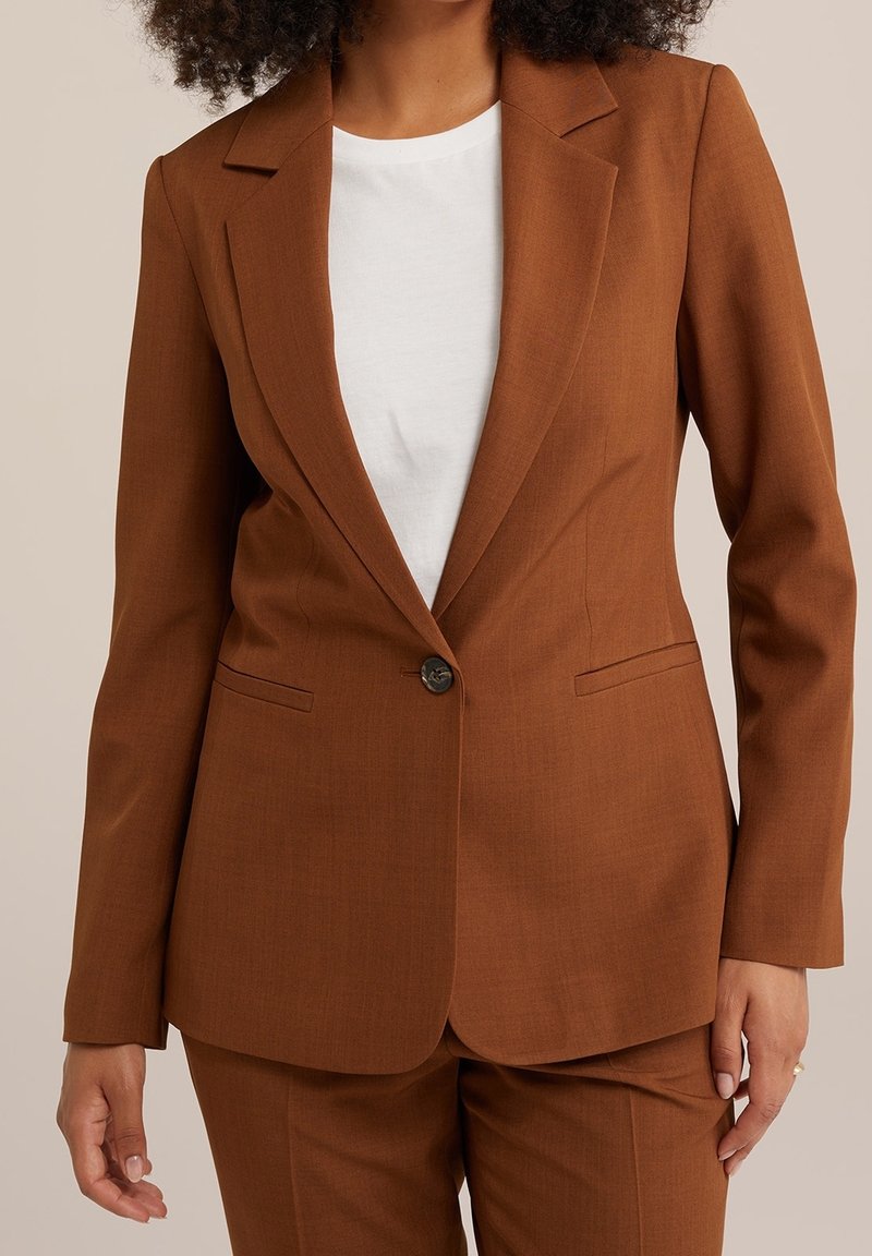 Brown blazer with a notched lapel and single button closure; features two side pockets and a tailored fit over a white shirt.