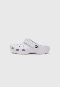 White clog with open ventilation holes, raised heel, molded structure, and a black logo accent on the side. Adjustable back strap for fit.