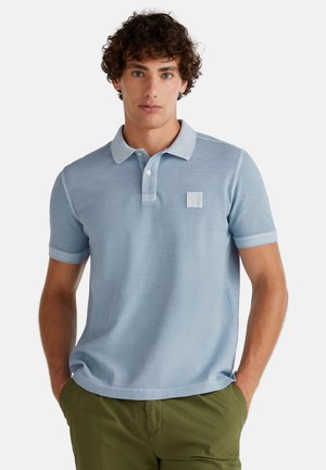 Light blue polo shirt in soft cotton with a collared neckline and a small pocket accent, paired with olive green shorts.