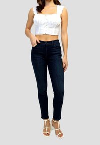 Top corto blanco con tirantes con volantes, combinado con pantalones skinny azul oscuro y tacones blancos con tiras. Tejido suave y diseño ajustado.