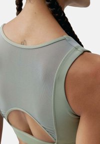 Svijetlo zelena sportska majica s mrežastim leđima, koja ima okrugli izrez i detalj izreza. Glatka tekstura s prilagođenim dizajnom.