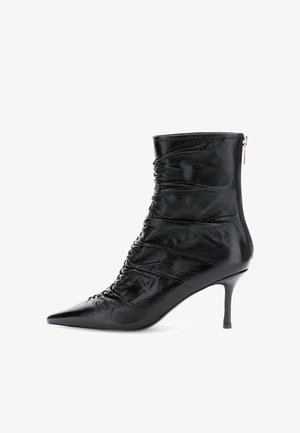 Bota de tobillo negra con puntera afilada, de cuero arrugado y un tacón slim de altura media, que cuenta con un cierre de cremallera en la parte trasera.