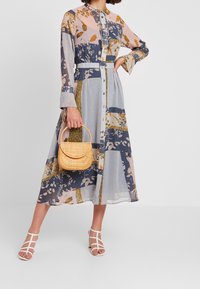 Robe longue à boutons avec un mélange de motifs floraux et géométriques dans des couleurs pastel et marine. Présente une taille cintrée et une jupe évasée.