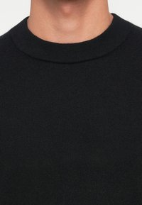 Black knit sweater with a round neck. The texture is smooth and uniform, featuring no visible patterns or accents.