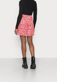 Röd blomsterprickig minikjol med volanglager, matchad med en svart långärmad topp och svarta kraftiga ankelskor.