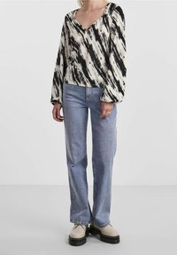 Långärmad blus i svart och krämfärgad abstrakt mönster, med V-ringning och rynkade axelsömmar, tillsammans med ljusblå raka jeans.