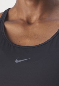 Czarny sportowy top na ramiączka wykonany z miękkiej tkaniny. Posiada okrągły dekolt oraz małe szare logo Nike z przodu. Gładka tekstura.