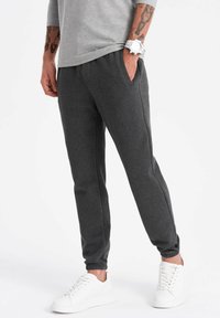 Joggers de color gris oscuro con cinturilla elástica, bolsillos laterales y puños acanalados. Combinados con zapatillas blancas y una camiseta gris casual.