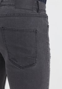 Zwarte denim jeans met een standaard achterzak en lichte rafelingen aan de rechterzijnaad. Gladde textuur met versterkte stiknaden.