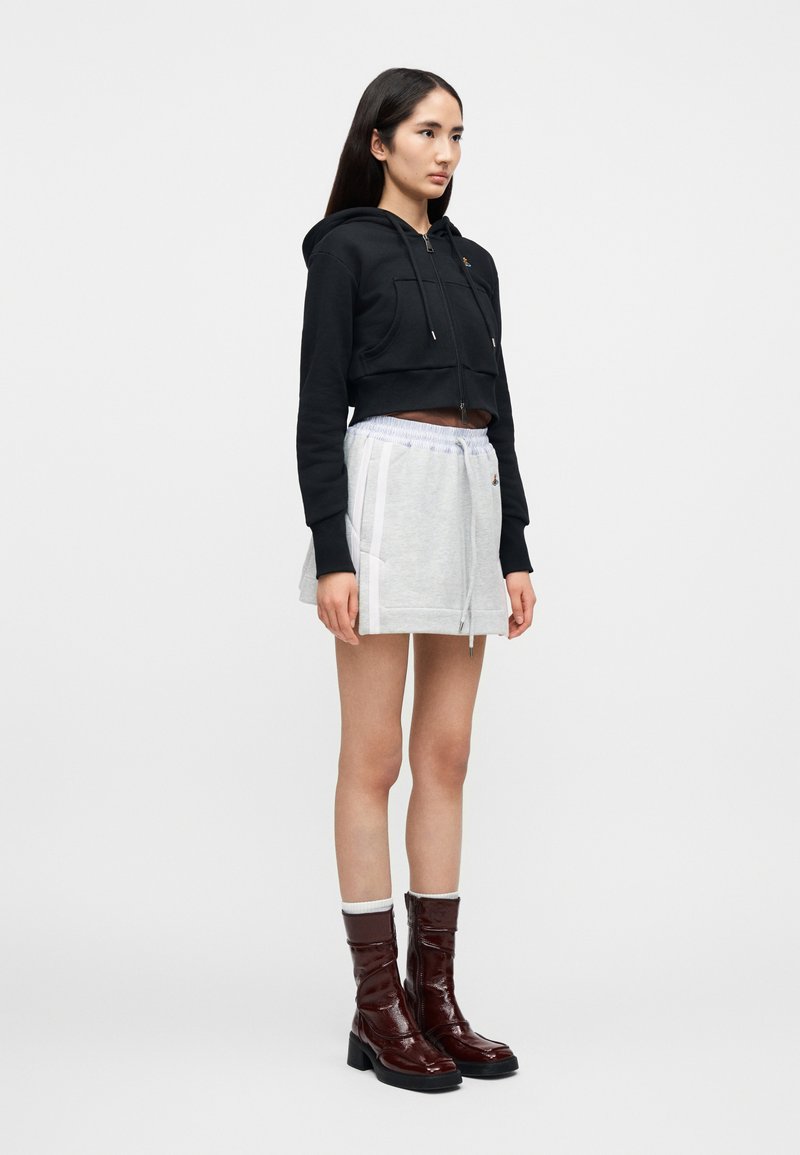 Sweat à capuche noir court avec poches avant, associé à un skort gris à cordon de serrage avec des bandes blanches sur les côtés. Bottines marron brillantes.