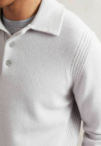Polo lavorato a maglia grigio chiaro con colletto strutturato, due bottoni argentati e pannelli laterali testurizzati. Materiale morbido e liscio con leggere righe. 