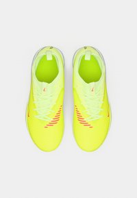 Jasnożółte buty sportowe z teksturowaną cholewką, różowymi akcentami i sznurowadłami. Charakteryzują się zaokrąglonym noskiem i amortyzowaną podeszwą.