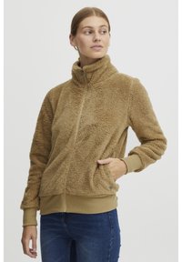 Pruun pehme fleece-jakk koos kõrge kaelusega, lukuga kinnitamise ja küljetaskutega. Omab soonikust mansette ja alumist serva ning pehmet tekstuuri.