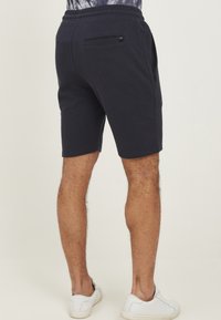 Marineblauwe sportshorts met een elastische tailleband en een zak met ritssluiting aan de achterkant. Gemaakt van een zachte, gestructureerde stof, eindigend net boven de knie.