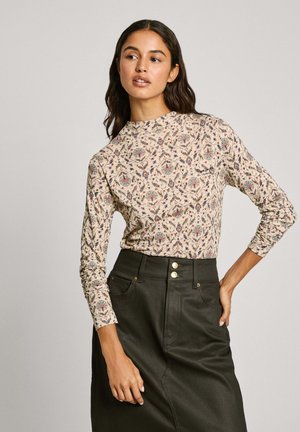 Blusa de manga larga en crema con un patrón floral en azul, rojo y verde. Combinada con una falda oscura que presenta botones visibles y bolsillos.