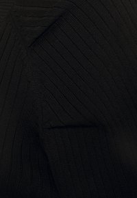 Tissu en tricot noir à côtes avec une surface texturée, présentant un détail de panneau triangulaire distinct sur un côté.