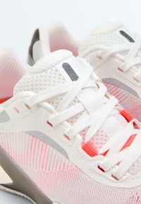 Chaussures de sport en mesh respirant blanc et rose avec des lacets blancs et des accents gris, montrant des détails en gros plan à l'avant et sur les côtés.