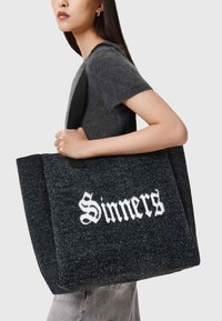 Grå tote-väska med svarta handtag, prydd med ordet "Sinners" i vit kursiv stil. Enkel, strukturerad form med en texturerad yta.