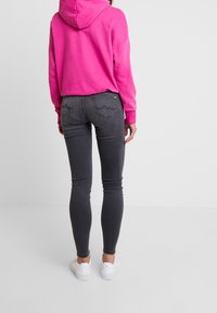 Jeans ajustados grises combinados con una sudadera rosa. Los jeans presentan bolsillos traseros distintivos y un sutil detalle de costura. Zapatillas completan el atuendo.