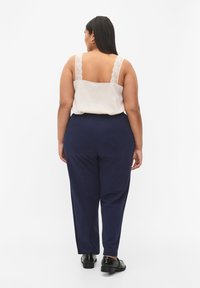 Beige tank top with lace straps and navy trousers, featuring a relaxed fit and smooth texture, paired with shiny black shoes.