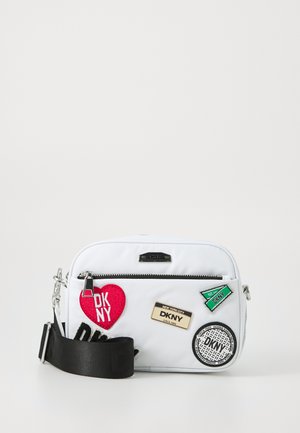 Hvit stoff crossbody-veske med flere lapper, inkludert et rødt hjerte og DKNY-logo, samt en svart justerbar stropp. Sølv glidelås og detaljer.