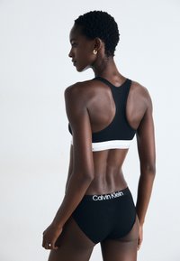 Svart sportsbra med hvit kant, racerback-design. Høyt midje svarte truser med logo på midjebåndet. Glatt tekstur, tettsittende stil.