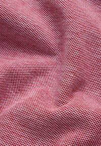 Czerwono-biała tkanina pleciona z teksturowanym wzorem w kratę, charakteryzująca się gładkim, elastycznym spadkiem. Ogólnie rzecz biorąc, jest to trwały materiał.