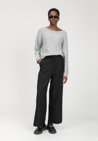 Maglione grigio leggero con dettagli scintillanti sottili; pantaloni neri a gamba larga; scarpe nere chunky con accentuazione in catena.