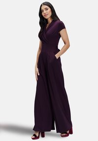 Purple jumpsuit with a v-neckline, short sleeves, and wide legs. Smooth fabric, featuring side pockets and a fitted waist.