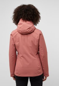 Waterdichte roze jas met capuchon, aansluitend ontwerp, gladde textuur en naadtoesichting, bekeken vanuit de achtergrond.