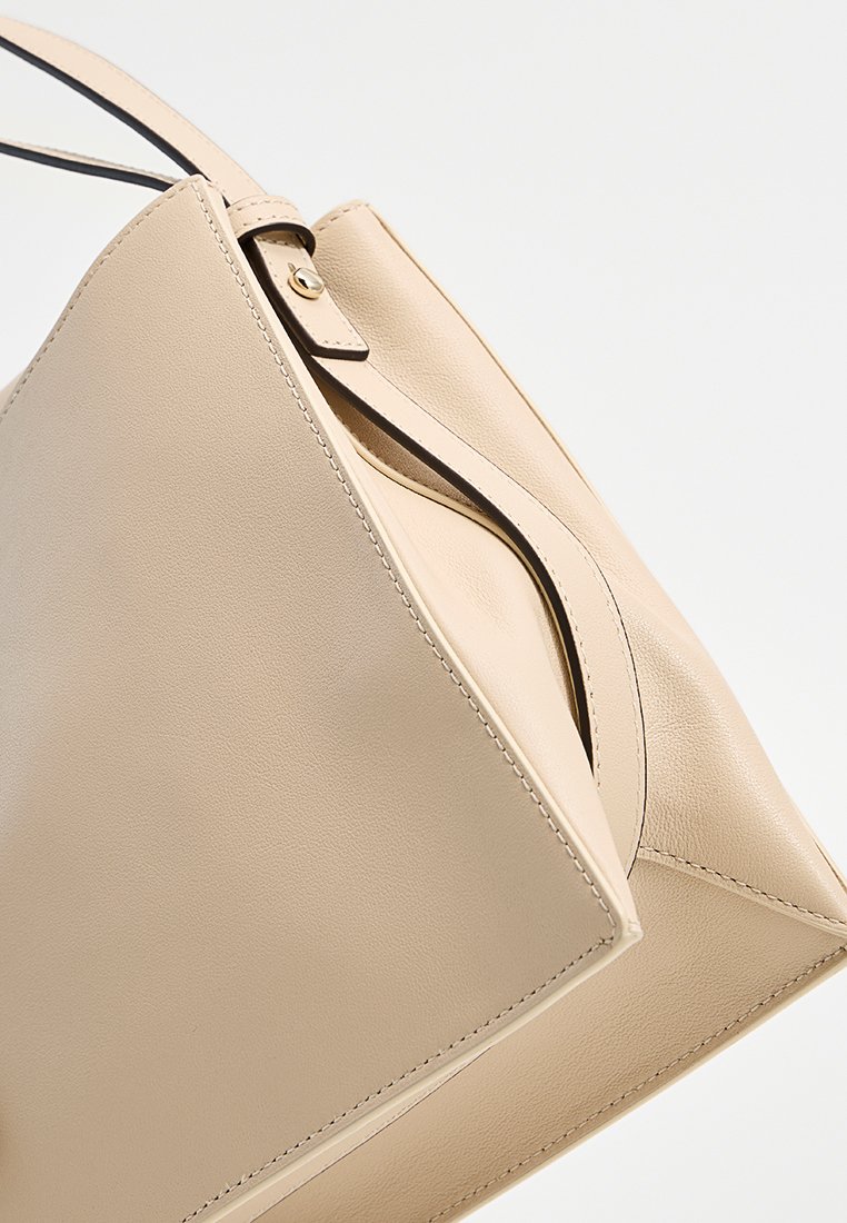 Borsa tote in pelle beige con un design strutturato, manico superiore e cuciture a contrasto. Presenta un'apertura unica con dettaglio piegato.