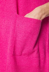Main dans la poche d'un pull tricoté rose vif montrant la texture et le détail du bord-côtes.