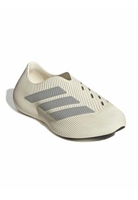 Ανοιχτό μπεζ slip-on αθλητικό παπούτσι με υφή, τρεις γκρι ρίγες στο πλάι και μικρές οπές αερισμού κοντά στην περιοχή των δαχτύλων.